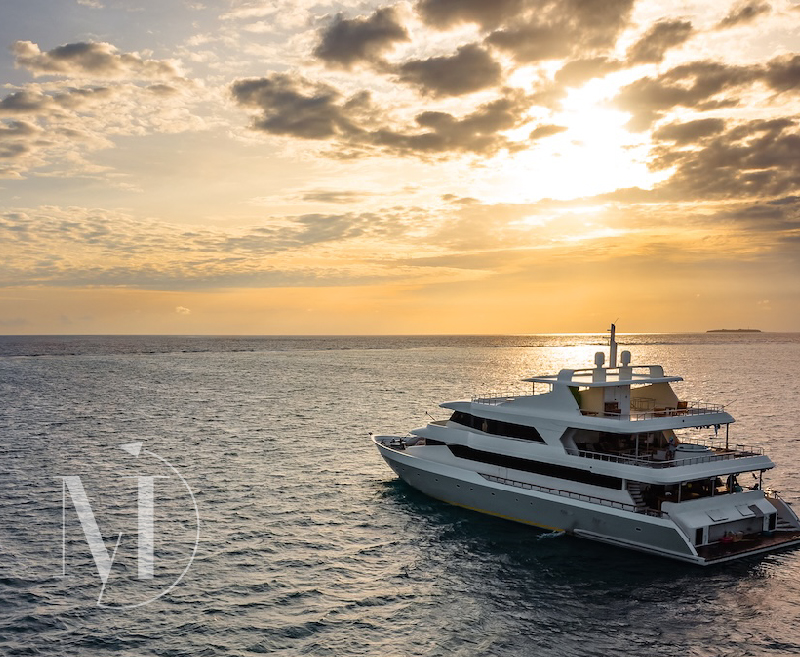 Panoramic view of a large white yacht sailing across tranquil waters under a golden, cloudy sky, representing the ultimate luxury getaway and bespoke vacation in exotic destinations.