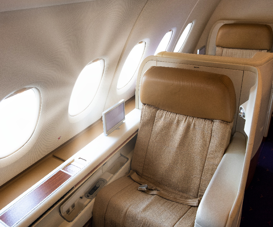 A spacious, first-class airline cabin interior with plush, beige seating and individual entertainment screens, highlighting the luxurious comfort and premium travel experience offered by leading airlines.