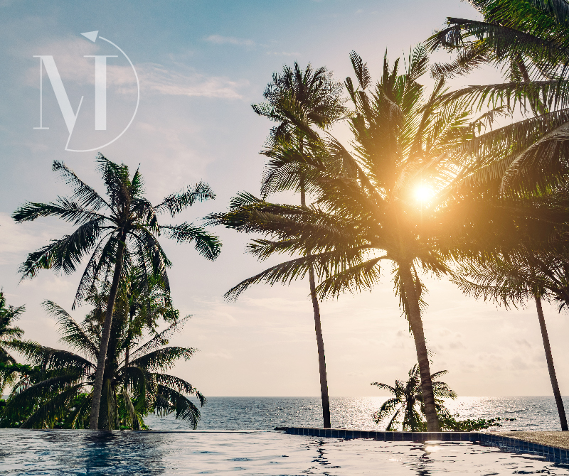 Tropical view of palm trees silhouetted against a brilliant sunset, with a luxury infinity pool overlooking the ocean, promoting exotic getaways and unparalleled relaxation.